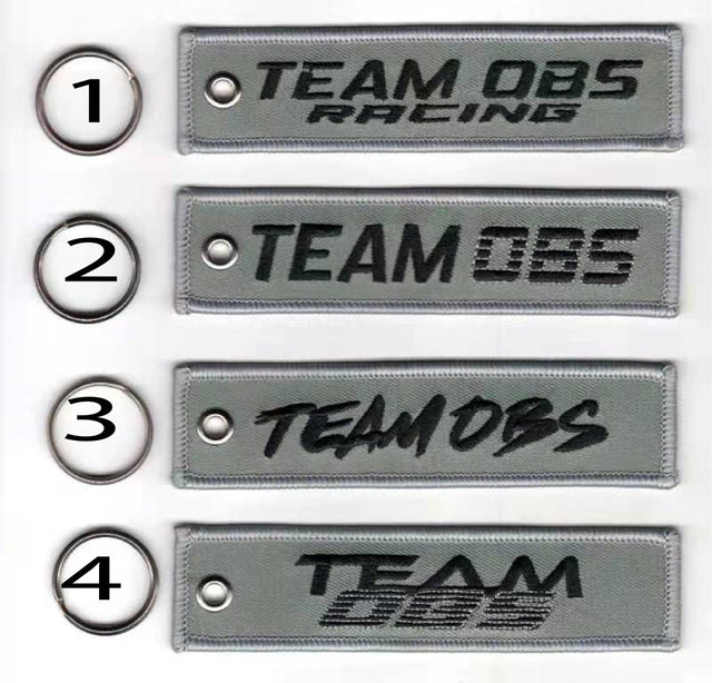 Team OBS flight tag keychains in grey with embroidered logos and metal keyrings