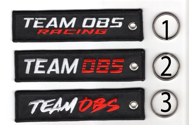 Team OBS flight tag keychains in black with embroidered logos and metal keyrings